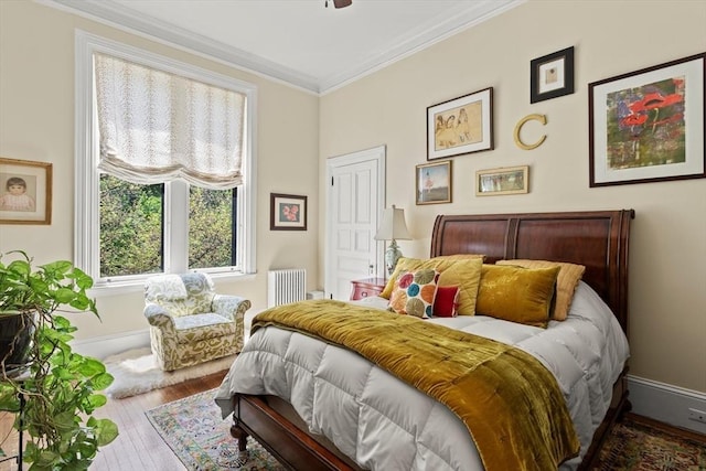bedroom featuring radiator, wood finished floors, crown molding, and baseboards