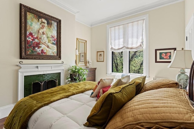 bedroom featuring ornamental molding, a tiled fireplace, and wood finished floors