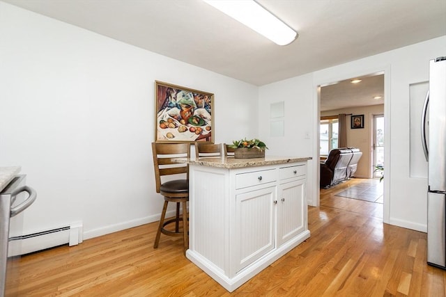 kitchen featuring white cabinets, a kitchen breakfast bar, baseboard heating, light stone countertops, and light wood-type flooring