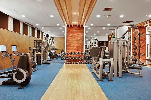 exercise room with carpet floors, recessed lighting, visible vents, and wood walls