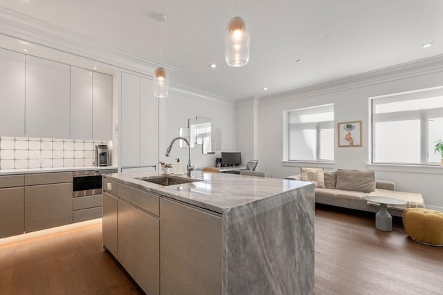 kitchen with a center island with sink, ornamental molding, open floor plan, wood finished floors, and a sink