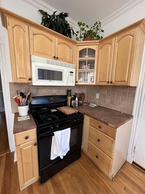 kitchen featuring black gas range oven, backsplash, light hardwood / wood-style flooring, and ornamental molding