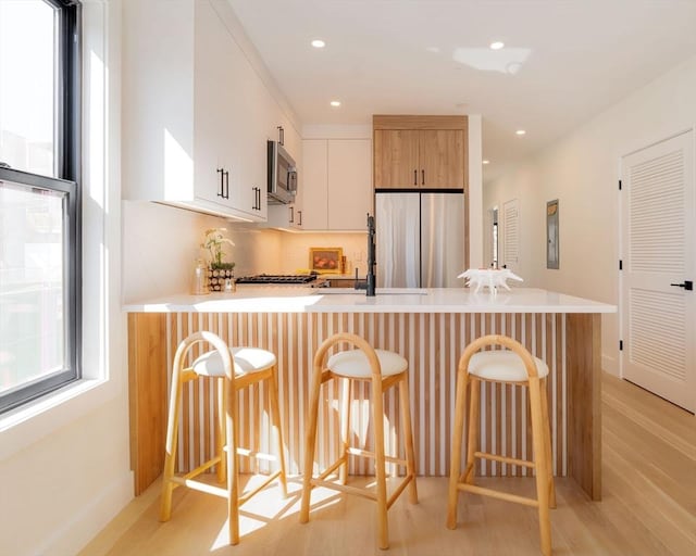 kitchen featuring a peninsula, light countertops, appliances with stainless steel finishes, a kitchen bar, and backsplash