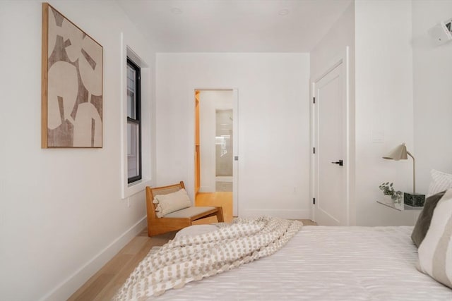 bedroom with connected bathroom, baseboards, and light wood-style floors