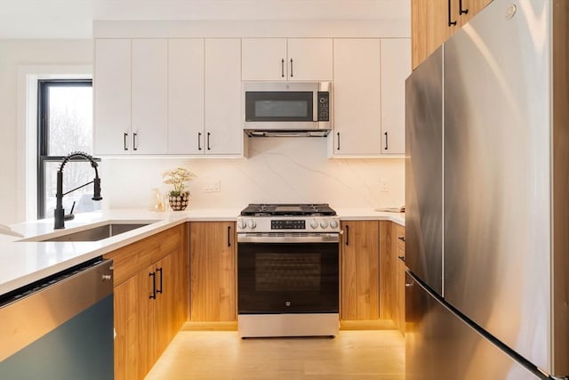 kitchen with a sink, stainless steel appliances, light wood finished floors, and light countertops