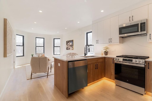 kitchen featuring a peninsula, a sink, light countertops, appliances with stainless steel finishes, and open floor plan