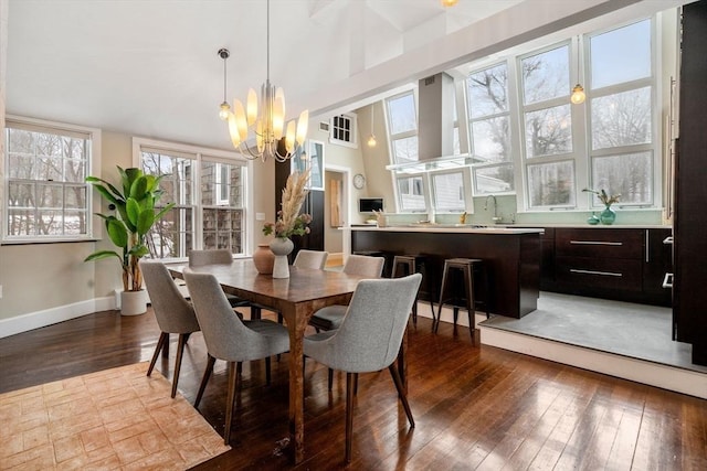 dining area featuring a notable chandelier, a towering ceiling, baseboards, and wood finished floors