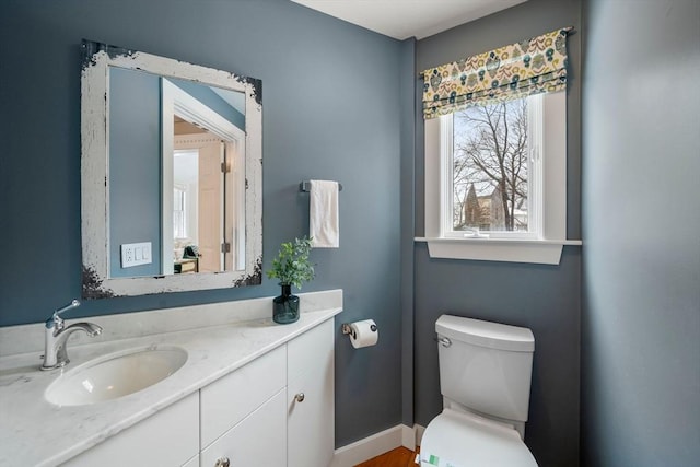 half bathroom featuring toilet, vanity, and baseboards