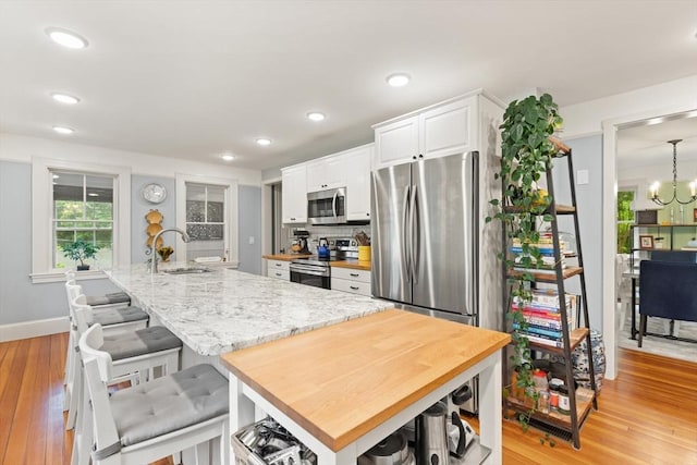 965 Greenville Ave, Smithfield, RI 02828 - kitchen with appliances with stainless steel finishes, white cabinetry, light wood-type flooring, an island with sink, and light stone counters
