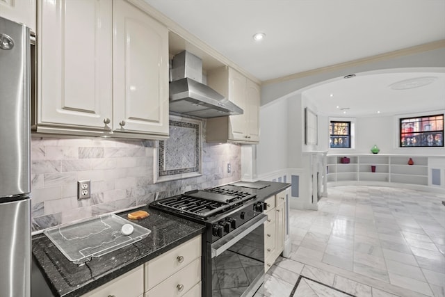 kitchen featuring stainless steel appliances, crown molding, dark stone countertops, and wall chimney range hood