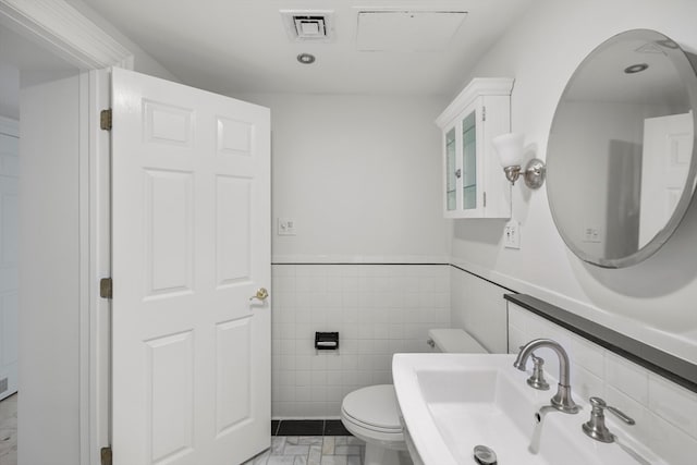 bathroom with toilet, sink, and tile walls