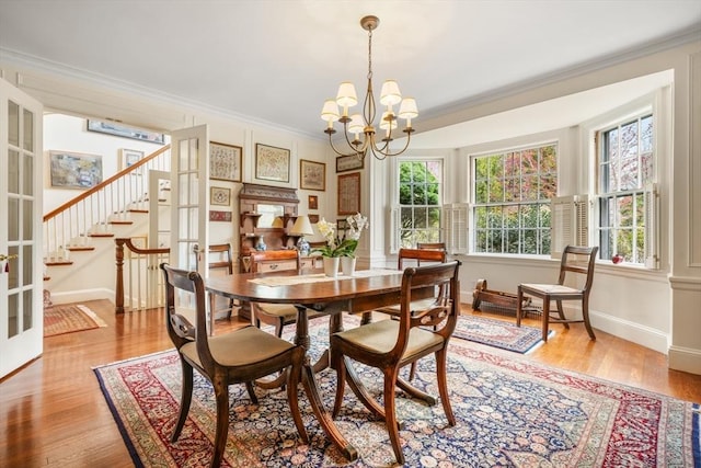 dining room with a chandelier, crown molding, plenty of natural light, light wood finished floors, and stairway