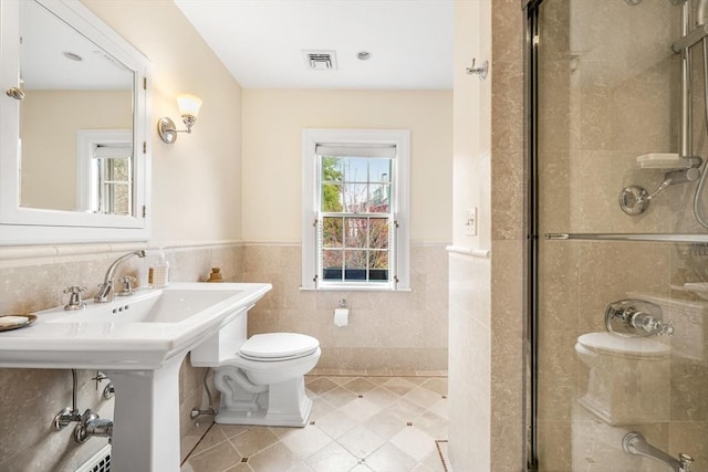 bathroom with toilet, a stall shower, tile patterned flooring, wainscoting, and tile walls