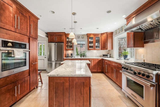 kitchen featuring high end appliances, wall chimney range hood, glass insert cabinets, a kitchen island, and light tile patterned floors