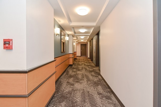 corridor with a tray ceiling and dark colored carpet