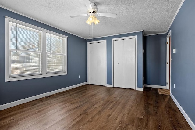 unfurnished bedroom featuring two closets, dark hardwood / wood-style flooring, ceiling fan, crown molding, and a textured ceiling