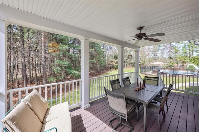 wooden terrace with a yard, outdoor dining space, a ceiling fan, and fence
