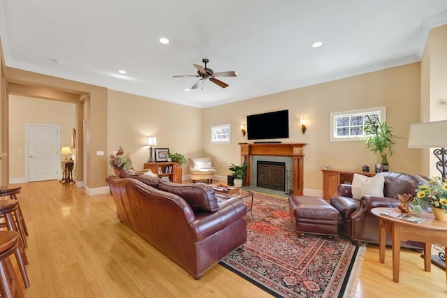 living area with a wealth of natural light, a fireplace, light wood-type flooring, and a ceiling fan