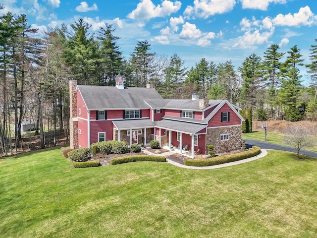 back of property with a porch, a chimney, stone siding, and a lawn