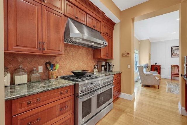 kitchen featuring under cabinet range hood, light wood-style flooring, range with two ovens, and decorative backsplash