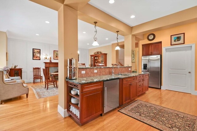 kitchen featuring light wood-style floors, brown cabinets, dark stone counters, appliances with stainless steel finishes, and a sink