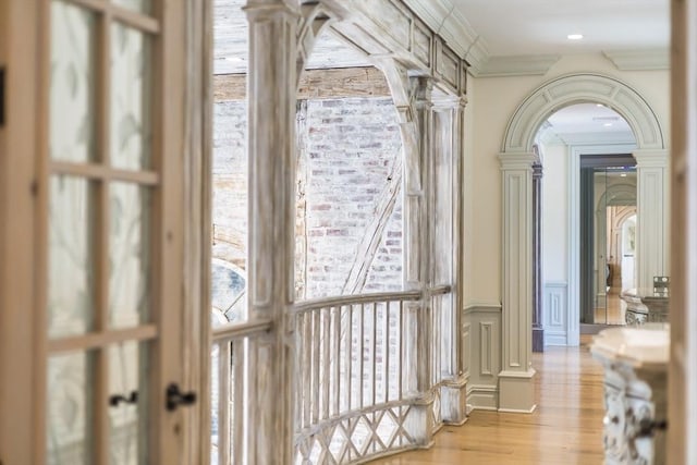 corridor featuring light wood-type flooring, ornamental molding, and ornate columns