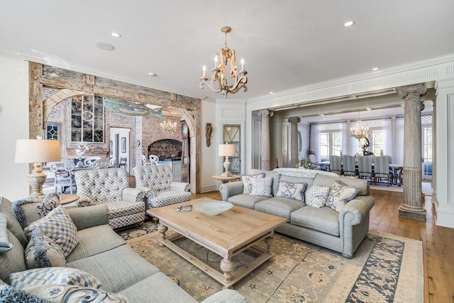 living room featuring an inviting chandelier, ornamental molding, ornate columns, and light wood-type flooring