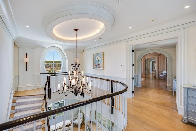 hallway featuring ornamental molding, light hardwood / wood-style flooring, a notable chandelier, and a tray ceiling