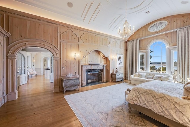 bedroom featuring wooden walls, a fireplace, lofted ceiling, hardwood / wood-style flooring, and a notable chandelier