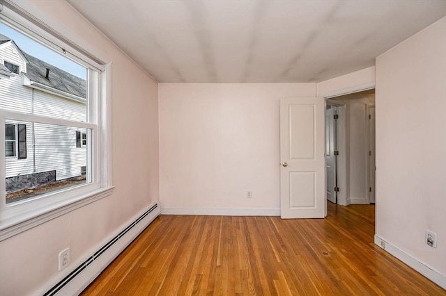 spare room featuring a baseboard heating unit, light wood finished floors, baseboards, and a wealth of natural light