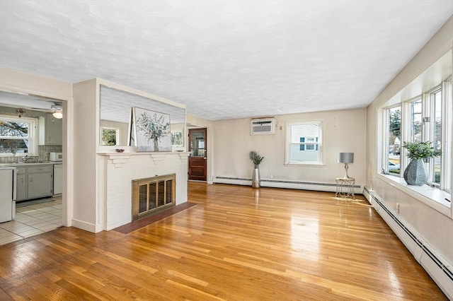 unfurnished living room with a baseboard heating unit, light wood-style flooring, a fireplace, a textured ceiling, and a sink