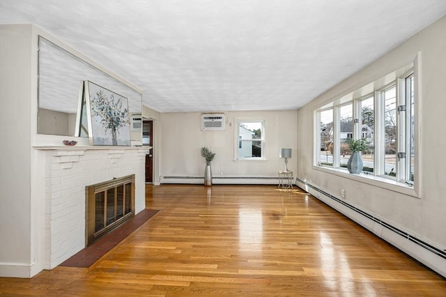 unfurnished living room featuring a baseboard radiator, a brick fireplace, an AC wall unit, and light wood finished floors