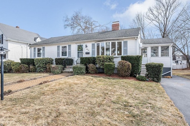 view of front facade featuring a shingled roof, a front yard, and a chimney