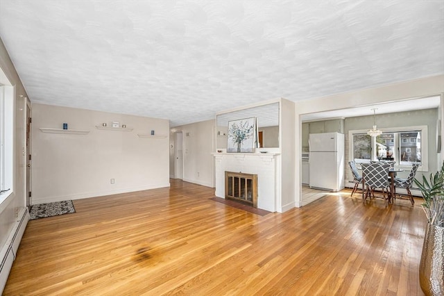 unfurnished living room with a baseboard radiator, a fireplace, a textured ceiling, a baseboard heating unit, and light wood-type flooring