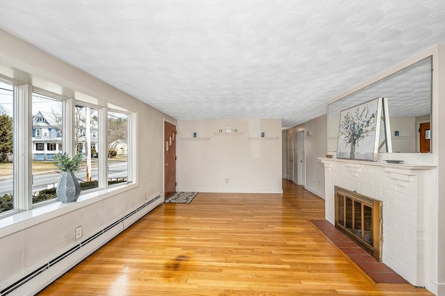 unfurnished living room featuring a brick fireplace, baseboards, wood finished floors, a textured ceiling, and a baseboard radiator