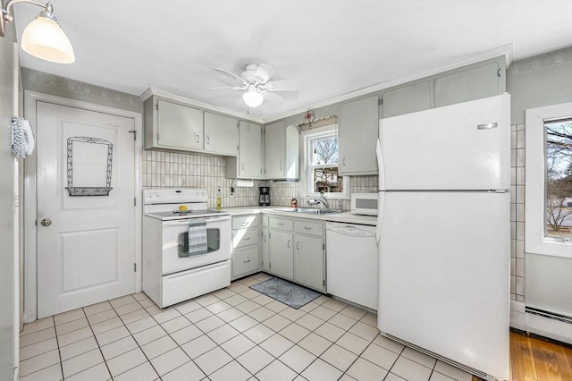 kitchen featuring white appliances, a baseboard radiator, ceiling fan, a sink, and light countertops