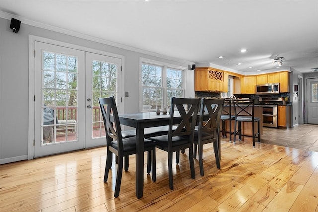 dining space featuring a healthy amount of sunlight, light wood-type flooring, ornamental molding, and french doors