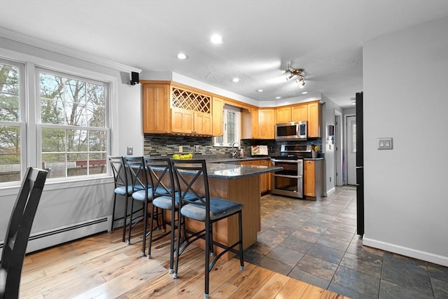 kitchen with a breakfast bar area, a peninsula, baseboards, appliances with stainless steel finishes, and tasteful backsplash