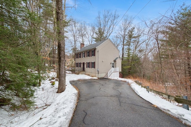 view of snow covered exterior with driveway and a chimney