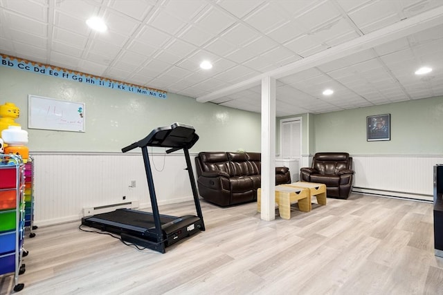 exercise area featuring a baseboard heating unit, a wainscoted wall, baseboard heating, and wood finished floors