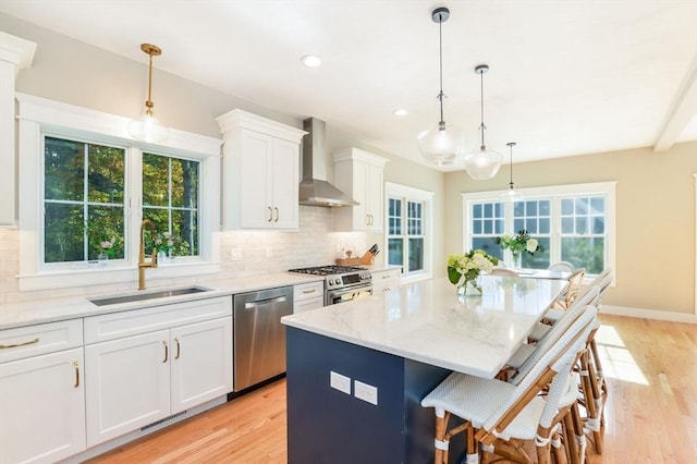 kitchen featuring white cabinetry, appliances with stainless steel finishes, decorative light fixtures, wall chimney range hood, and a kitchen island