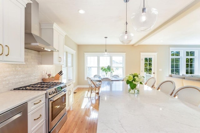 kitchen with stainless steel appliances, pendant lighting, light stone countertops, wall chimney exhaust hood, and white cabinets