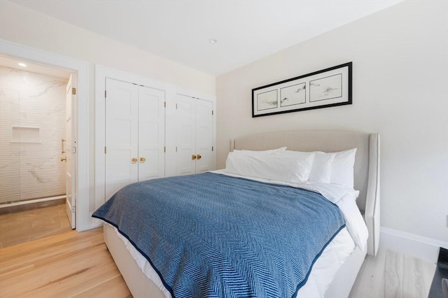 bedroom with two closets, baseboards, light wood-style flooring, and ensuite bathroom