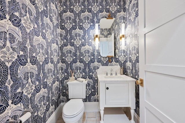 bathroom with vanity, baseboards, toilet, and wallpapered walls