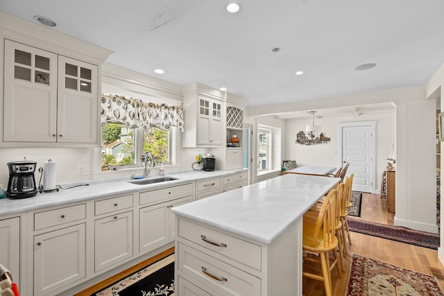 kitchen with a kitchen island, pendant lighting, sink, light hardwood / wood-style flooring, and white cabinets