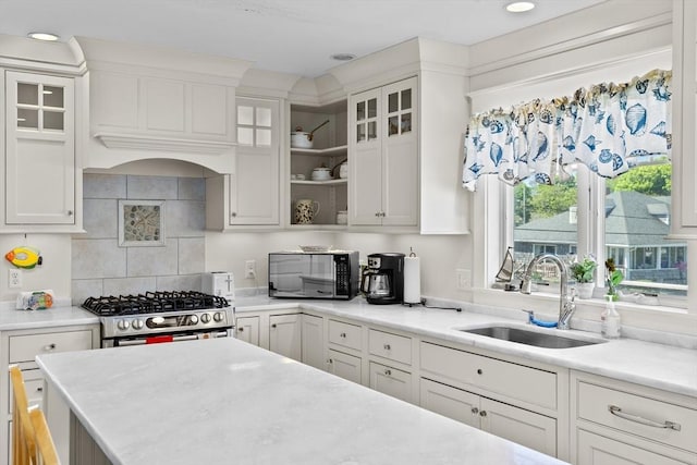 kitchen featuring sink, white cabinetry, backsplash, and stainless steel gas range oven