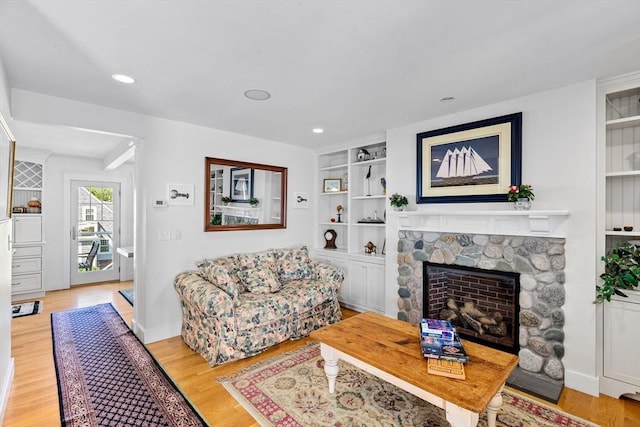 living room featuring built in features, light hardwood / wood-style flooring, and a stone fireplace