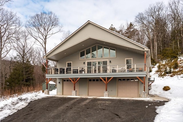 snow covered house with driveway, a balcony, and an attached garage