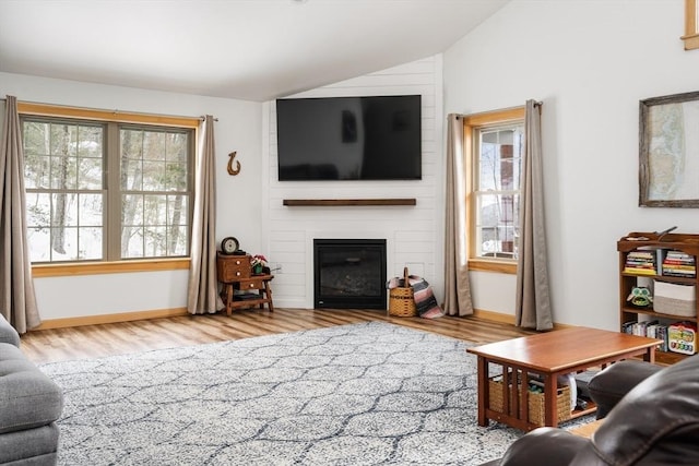 living room with lofted ceiling, a large fireplace, wood finished floors, and baseboards