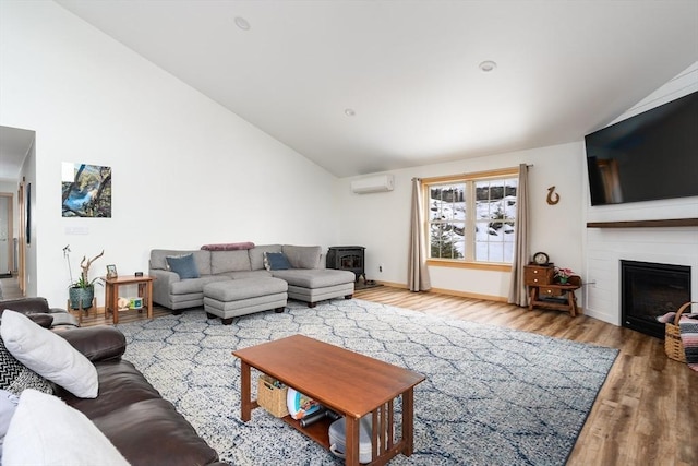 living room featuring a wall unit AC, wood finished floors, a wood stove, a fireplace, and high vaulted ceiling